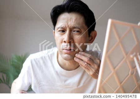 一位中年男子對著鏡子皺眉頭,嘴唇上長了皰疹,看起來很苦惱。 一位中年男子對著鏡子皺眉頭,嘴唇上長了皰疹,看起來很苦惱。 140495478