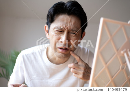 一位中年男子對著鏡子皺眉頭,嘴唇上長了皰疹,看起來很苦惱。 一位中年男子對著鏡子皺眉頭,嘴唇上長了皰疹,看起來很苦惱。 140495479