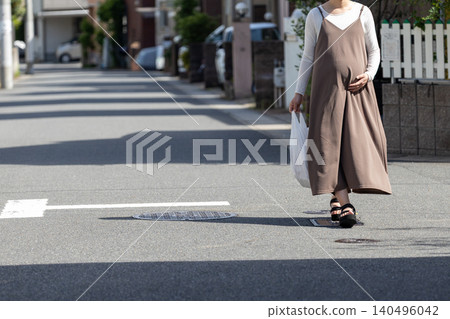 A pregnant woman walking through a residential area, carrying a shopping bag after returning from shopping. 140496042