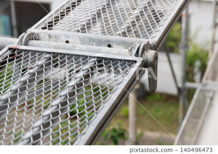 Close-up of the mesh-like treads used in scaffolding during exterior wall painting of houses. Close-up of the mesh-like treads used in scaffolding during exterior wall painting of houses. 140496473