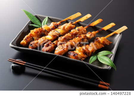 A savory grilled chicken dish served on a black plate, complete with chopsticks and a chopstick rest—a typical izakaya menu item. 140497228