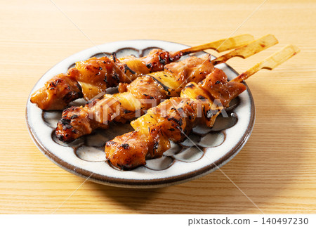 Three skewers of yakitori (grilled chicken skewers) with sauce, served on a wooden table in a Japanese-style dish. (Image of a home-style side dish). 140497230