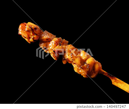 A single grilled chicken thigh with sauce, isolated against a black background, positioned at an elegant angle, is a cutout material. 140497247