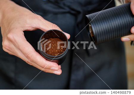 Hands holding manual grinder with fresh coffee grounds inside Hands holding manual grinder with fresh coffee grounds inside 140498879