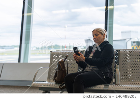 Woman Sitting in Airport Waiting Area Before Flight Departure Checking Her Phone Woman Sitting in Airport Waiting Area Before Flight Departure Checking Her Phone 140499205