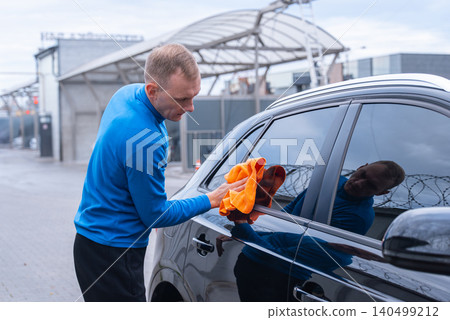 Concept of vehicle maintenance, wiping drying polishing car care cleanliness, modern contactless automated washing self services. Man cleans exterior of luxury car with microfiber rags. Automotive Concept of vehicle maintenance, wiping drying polishing car care cleanliness, modern contactless automated washing self services. Man cleans exterior of luxury car with microfiber rags. Automotive 140499212