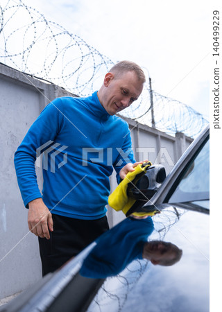 Concept of vehicle maintenance, wiping drying polishing car care cleanliness, modern contactless automated washing self services. Man cleans exterior of luxury car with microfiber rags. Automotive Concept of vehicle maintenance, wiping drying polishing car care cleanliness, modern contactless automated washing self services. Man cleans exterior of luxury car with microfiber rags. Automotive 140499229