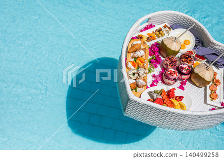 Heart-shaped floating breakfast basket with flowers in a turquoise pool, seen from above. Romantic honeymoon resort indulgence and luxury wellness travel concept for couples. Heart-shaped floating breakfast basket with flowers in a turquoise pool, seen from above. Romantic honeymoon resort indulgence and luxury wellness travel concept for couples. 140499258