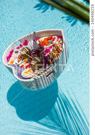 Aerial top-down view of an elegant floating breakfast in a clear turquoise swimming pool. Luxury resort wellness, honeymoon morning and indulgent tropical holiday lifestyle. Aerial top-down view of an elegant floating breakfast in a clear turquoise swimming pool. Luxury resort wellness, honeymoon morning and indulgent tropical holiday lifestyle. 140499259