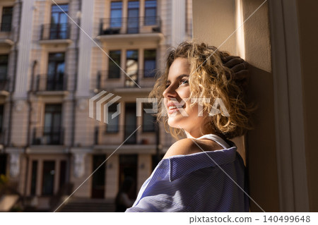 Woman stands near a building and smiles in the sunlight Woman stands near a building and smiles in the sunlight 140499648