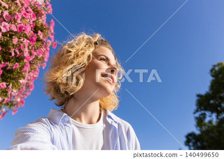 Person looks up with smile near blooming flowers and clear sky Person looks up with smile near blooming flowers and clear sky 140499650