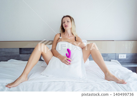 Young sexy woman in the bed holding in her hands a sex toy for adults Young sexy woman in the bed holding in her hands a sex toy for adults 140499736