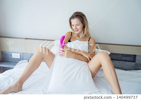 Young sexy woman in the bed holding in her hands a sex toy for adults Young sexy woman in the bed holding in her hands a sex toy for adults 140499737