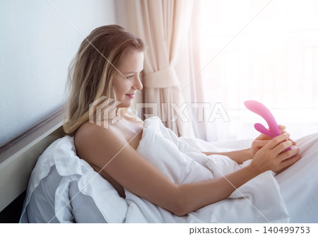 Young sexy woman in the bed holding in her hands a sex toy for adults Young sexy woman in the bed holding in her hands a sex toy for adults 140499753