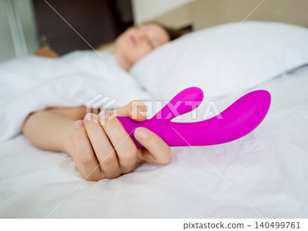 Young sexy woman in the bed holding in her hands a sex toy for adults Young sexy woman in the bed holding in her hands a sex toy for adults 140499761