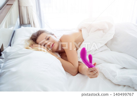 Young sexy woman in the bed holding in her hands a sex toy for adults Young sexy woman in the bed holding in her hands a sex toy for adults 140499767
