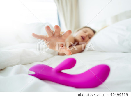 Young sexy woman in the bed holding in her hands a sex toy for adults Young sexy woman in the bed holding in her hands a sex toy for adults 140499769