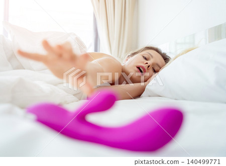 Young sexy woman in the bed holding in her hands a sex toy for adults Young sexy woman in the bed holding in her hands a sex toy for adults 140499771