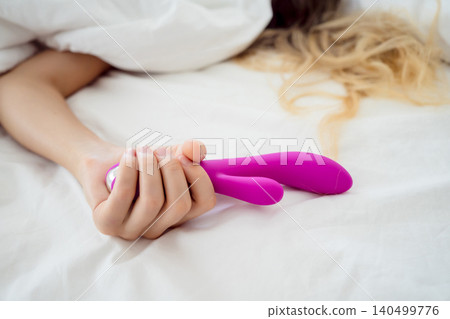 Young sexy woman in the bed holding in her hands a sex toy for adults Young sexy woman in the bed holding in her hands a sex toy for adults 140499776