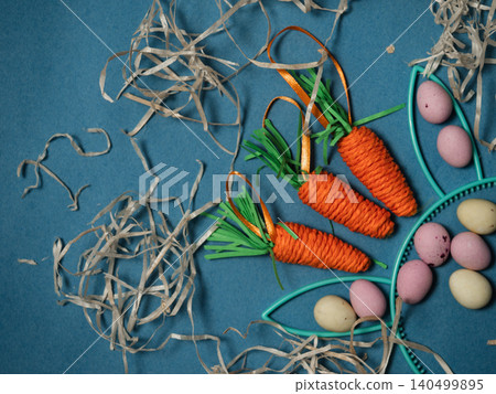 Easter display with bunny rabbit ears eggs and carrots blue background Easter display with bunny rabbit ears eggs and carrots blue background 140499895