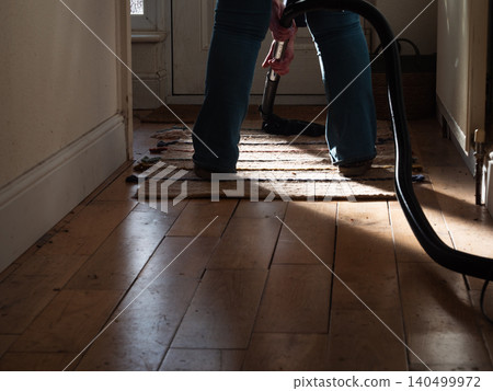 Woman using vacuum cleaner to clean up dust in home hallway Woman using vacuum cleaner to clean up dust in home hallway 140499972