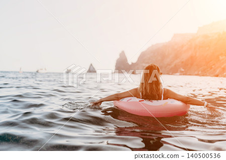 Woman, water, relaxation. Serene woman floating on a pink inflatable ring in the sea during golden hour. Woman, water, relaxation. Serene woman floating on a pink inflatable ring in the sea during golden hour. 140500536