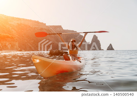 Kayaking Woman Ocean Coastline - Happy woman kayaking in the ocean near a rocky coastline during a summer day. Kayaking Woman Ocean Coastline - Happy woman kayaking in the ocean near a rocky coastline during a summer day. 140500540
