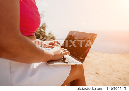 Laptop working freelancer typing on a silver computer while sitting on a rocky cliff by the sea at golden hour Laptop working freelancer typing on a silver computer while sitting on a rocky cliff by the sea at golden hour 140500545