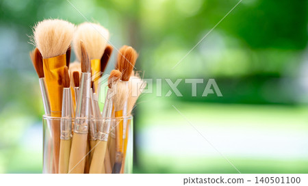 Set of various artist paintbrush in glass holder against a blurry green background of garden Set of various artist paintbrush in glass holder against a blurry green background of garden 140501100