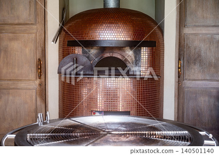 Empty modern wood fire pizza oven covered with copper bronze mosaic tiles with round BBQ grill rack Empty modern wood fire pizza oven covered with copper bronze mosaic tiles with round BBQ grill rack 140501140
