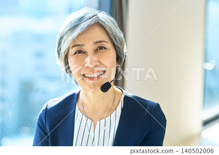 A gray-haired female operator, wearing a headset, smiles gently by the window. 140502006