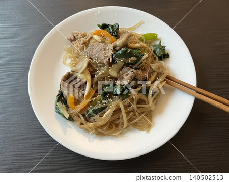 A vibrant plate of japchae featuring stir-fried glass noodles, colorful vegetables, and tender slices of meat, all coated in a savory-sweet soy-based sauce. A classic Korean favorite! A vibrant plate of japchae featuring stir-fried glass noodles, colorful vegetables, and tender slices of meat, all coated in a savory-sweet soy-based sauce. A classic Korean favorite! 140502513