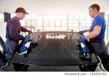 Automobile special workers replacing windscreen or windshield of a car in auto service station garage. Automobile special workers replacing windscreen or windshield of a car in auto service station garage. 140502793