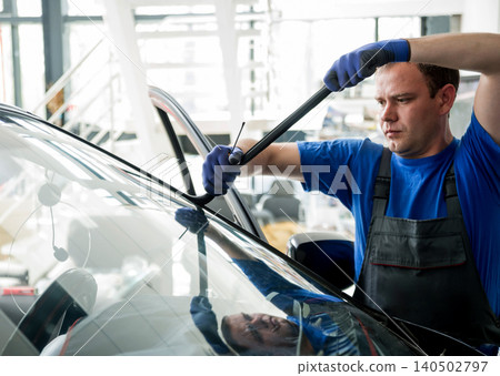 Automobile special workers remove old windscreen or windshield of a car in auto service station garage. Automobile special workers remove old windscreen or windshield of a car in auto service station garage. 140502797