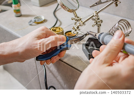 Hands soldering electronic component at workbench with helping hands tool and wire cutter Hands soldering electronic component at workbench with helping hands tool and wire cutter 140503372