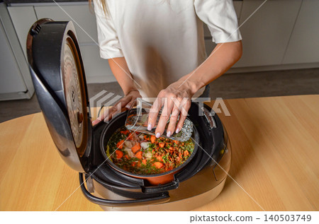 A Person Preparing a Healthy Vegetable Soup in a Slow Cooker, Featuring Fresh Ingredients Such as Carrots, Greens, and Herbs for a Nutritious Meal A Person Preparing a Healthy Vegetable Soup in a Slow Cooker, Featuring Fresh Ingredients Such as Carrots, Greens, and Herbs for a Nutritious Meal 140503749