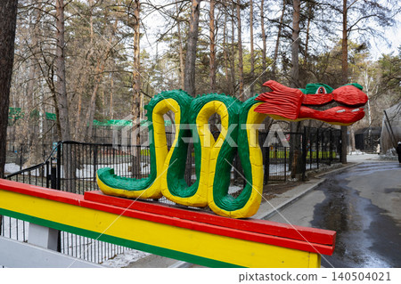 Colorful Wooden Snake Sculpture at a Park Amidst a Green Forest Pathway Captivating Visitors with Its Unique Design and Vivid Colors Colorful Wooden Snake Sculpture at a Park Amidst a Green Forest Pathway Captivating Visitors with Its Unique Design and Vivid Colors 140504021