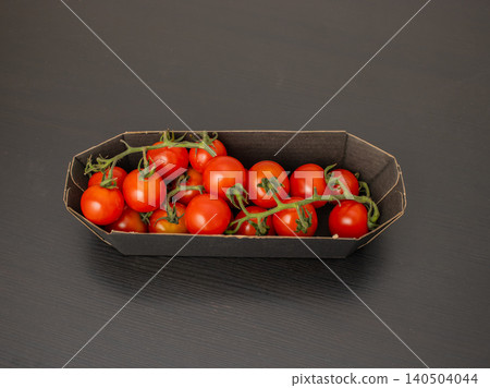 Cherry tomatoes on the vine in paper tray on dark table with copy space Cherry tomatoes on the vine in paper tray on dark table with copy space 140504044