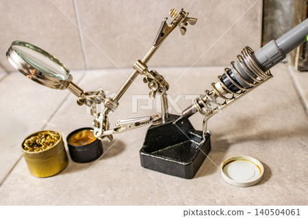 Soldering iron in stand with helping hands magnifier and solder on workbench for electronics repair Soldering iron in stand with helping hands magnifier and solder on workbench for electronics repair 140504061