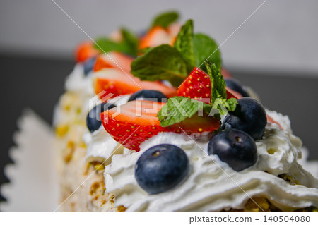 Dessert topped with whipped cream, strawberry, blueberry and mint in close-up Dessert topped with whipped cream, strawberry, blueberry and mint in close-up 140504080