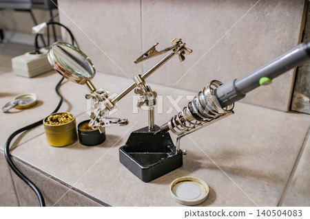 Soldering station with magnifying glass and helping hands tool on workbench for electronics repair Soldering station with magnifying glass and helping hands tool on workbench for electronics repair 140504083