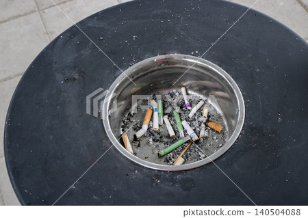 A Close-Up View of a Metal Ashtray Containing Discarded Cigarette Butts and Ashes with Grey Background A Close-Up View of a Metal Ashtray Containing Discarded Cigarette Butts and Ashes with Grey Background 140504088