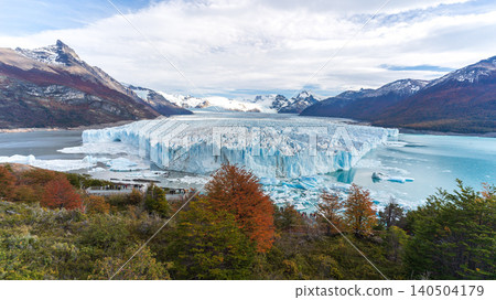 Glacier ice field in mountain lake landscape with snowy peak, autumn forest, and cloudy sky Glacier ice field in mountain lake landscape with snowy peak, autumn forest, and cloudy sky 140504179