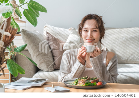 Stylish young Asian woman eating at the living room table Stylish young Asian woman eating at the living room table 140504401