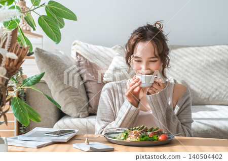 Stylish young Asian woman eating at the living room table Stylish young Asian woman eating at the living room table 140504402