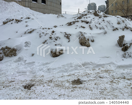 A Winter Landscape Featuring a Snow-Covered Terrain with Boulders and Urban Background, Capturing the Essence of Cold Climates and Seasonal Change A Winter Landscape Featuring a Snow-Covered Terrain with Boulders and Urban Background, Capturing the Essence of Cold Climates and Seasonal Change 140504440