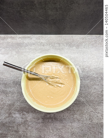 Creamy Batter Mixture Whisked to Perfection in a Light Yellow Bowl on a Textured Surface, Ready for Baking or Cooking Delicious Treats Creamy Batter Mixture Whisked to Perfection in a Light Yellow Bowl on a Textured Surface, Ready for Baking or Cooking Delicious Treats 140504465