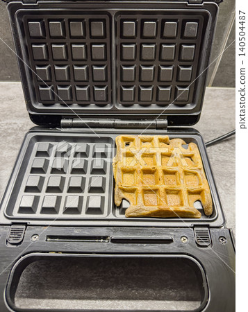 Golden Brown Waffle Cooking in a Modern Electric Waffle Maker with a Clean Design, Ideal for Breakfast or Snack Time at Home Golden Brown Waffle Cooking in a Modern Electric Waffle Maker with a Clean Design, Ideal for Breakfast or Snack Time at Home 140504487