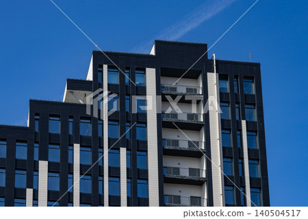 A Modern High-Rise Building Soaring Against a Clear Blue Sky with a Contemporary Architectural Design Showcasing Sleek Lines and Geometric Shapes. 140504517