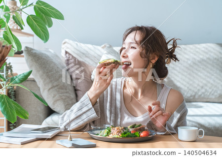 Stylish young Asian woman eating at the living room table 140504634